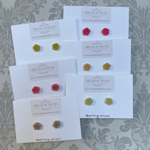 May include: Six pairs of sterling silver flower stud earrings displayed on white cards. The earrings are available in green, pink, and brown.