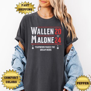 May include: A dark grey t-shirt with the text "Wallen 20 Malone 24" in white with a red star. The text "Teamwork makes the dream work" is below in white with a guitar icon on each side.