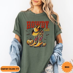 K&ouml;nnte beinhalten: Gr&uuml;nes T-Shirt mit einem Aufdruck eines Cowboyhutes und Stiefeln mit Blumenmustern. Der Text "Howdy Fall" ist auf dem Shirt gedruckt.