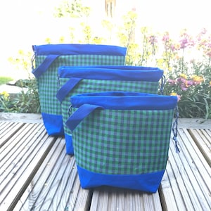 May include: Three blue and green gingham drawstring bags with blue handles. The bags are lined up in order of size, with the largest bag at the back and the smallest bag at the front.
