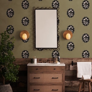 May include: A bathroom scene featuring a wooden vanity with a marble countertop, a mirror with a decorative frame, and sconces. The wall is olive green with a floral pattern. A towel rack and a small stool are also visible.