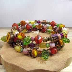 May include: A multi-strand bracelet with a variety of colorful beads. The bracelet features red, orange, yellow, green, and purple beads, with some shaped like leaves and pumpkins. The bracelet is displayed on a wooden surface.