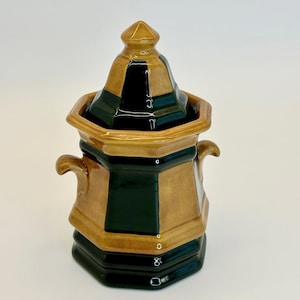 May include: A brown and green ceramic sugar bowl with a lid. The bowl has a geometric design and two handles.