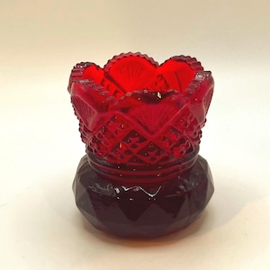 Op de afbeelding: Een robijnrode glazen tandenstokerhouder met een ruitpatroon en een geschulpte rand. De basis heeft een donkere, facetvorm. Dit vintage decoratie-item komt waarschijnlijk uit het begin van de 20e eeuw.