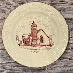 Könnte beinhalten: Cremefarbene Zierteller mit Goldrand. Der Teller zeigt eine sepiafarbene Illustration einer Kirche mit hohem Turm. Der Text "First Methodist Church, Sumner, Missouri" steht darunter. Der Teller hat einen floral geprägten Rand.