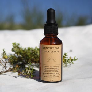 May include: A brown glass bottle of Desert Sun Face Serum with a black dropper. The label lists ingredients including creosote, golden jojoba oil, and rosehip oil. The bottle is 1 fl oz.