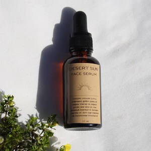 May include: A brown glass bottle of Desert Sun Face Serum with a black dropper. The label features the product name and a sun graphic. The bottle contains 1 fl oz of serum. The image is set against a white background.