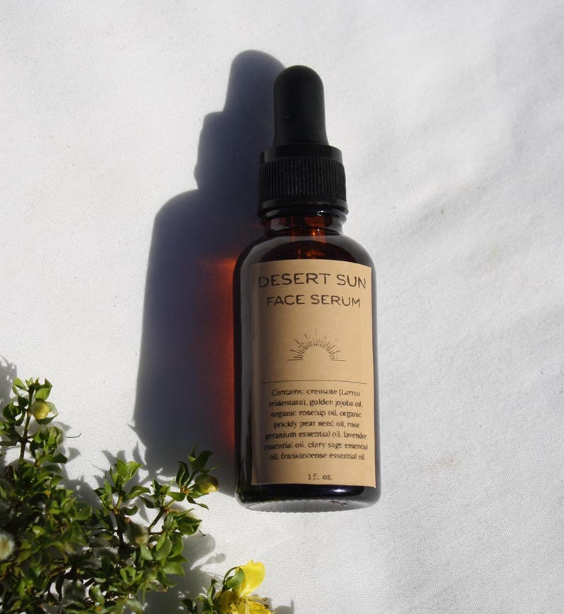 May include: A brown glass bottle of Desert Sun Face Serum with a black dropper. The label features the product name and a sun graphic. The bottle contains 1 fl oz of serum. The image is set against a white background.