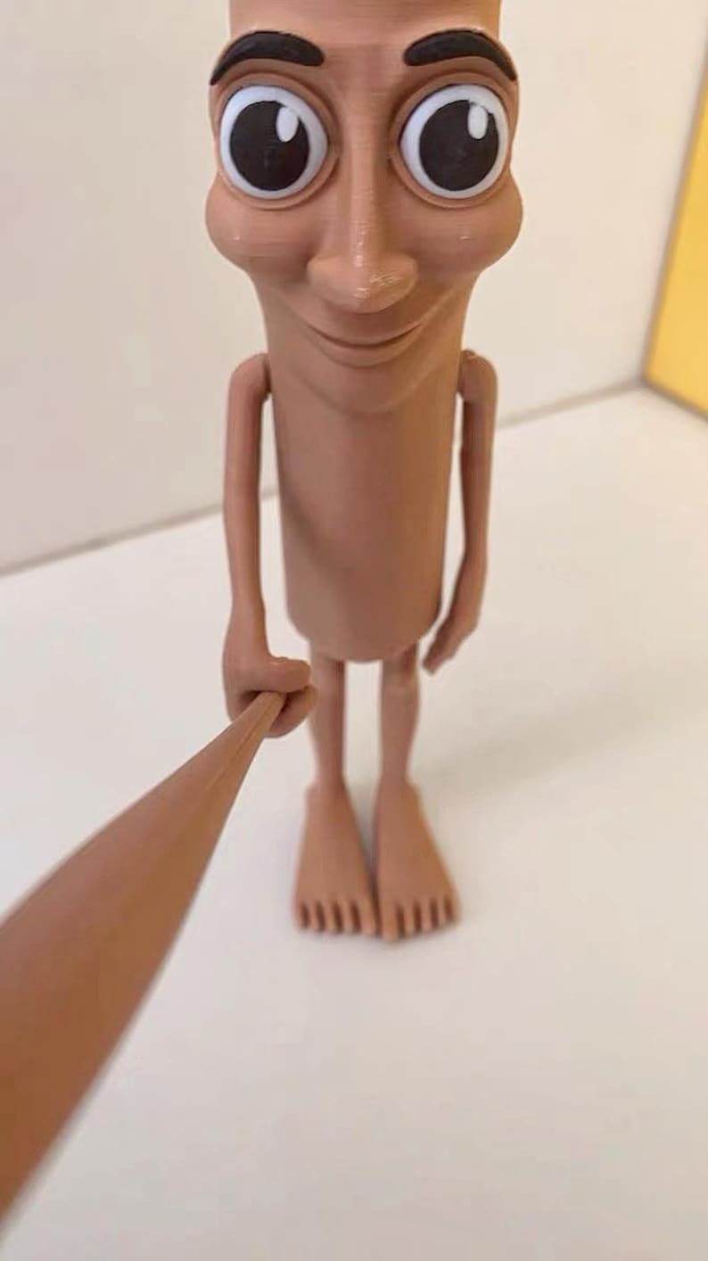 May include: A brown figurine of a person with large eyes and a wide smile. The figurine is holding a long, thin stick in its hand.