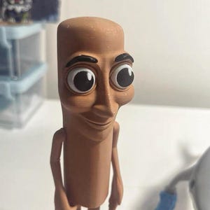 May include: A brown figurine of a person with large eyes and a smile. The figurine is made of plastic and has a cartoonish appearance.