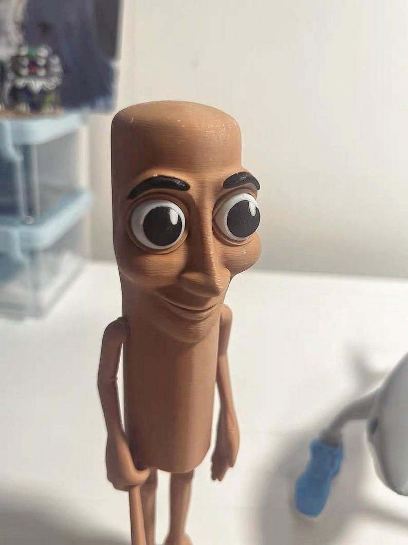 May include: A brown figurine of a person with large eyes and a smile. The figurine is made of plastic and has a cartoonish appearance.