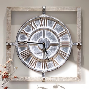 May include: A large, round, white and silver metal clock face with Roman numerals and black hands, framed in a square, distressed wood frame.