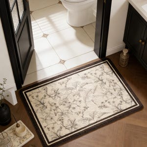May include: A rectangular bathroom rug with a beige background and a dark brown border. The rug features a botanical pattern in shades of brown and beige. The rug is placed in front of a bathroom door.