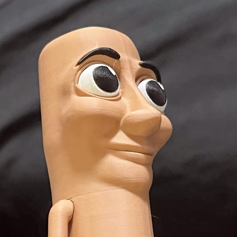 May include: A brown, humanoid figure with a large, round head and a long, thin neck. The figure has large, black eyes and a slightly open mouth, giving the impression of a smile. The figure is made of a smooth, textured material.