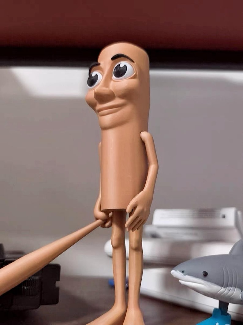 May include: A tan-colored figurine with a human-like face and large eyes. The figurine has long, thin legs and is holding a stick in its hands.