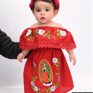 May include: A red off-the-shoulder dress with white and red floral embroidery. The dress features a depiction of the Virgin Mary in the center. The dress is worn by a baby girl with a red headband.