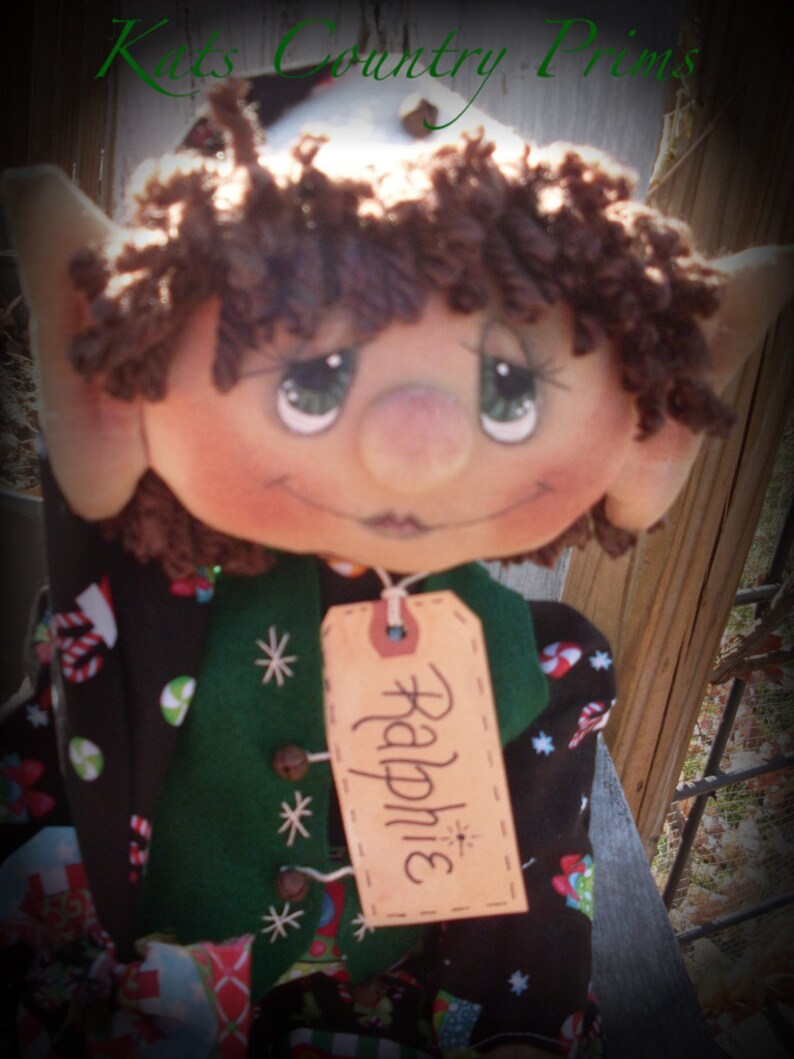 Pu&ograve; includere: Una bambola di elfo fatta a mano con capelli in lana marrone, un gilet verde e un'etichetta con il nome "Raphine".
