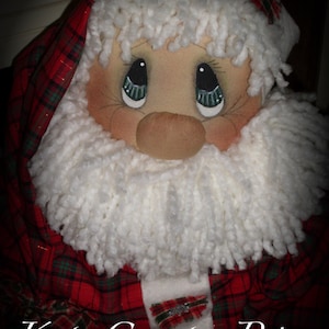 May include: A handmade Santa Claus doll with a red and green plaid outfit and a white fluffy beard. The doll has painted eyes and a rosy nose.