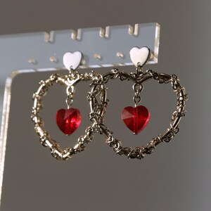 May include: A pair of gold heart-shaped earrings with dangling red heart-shaped crystals.