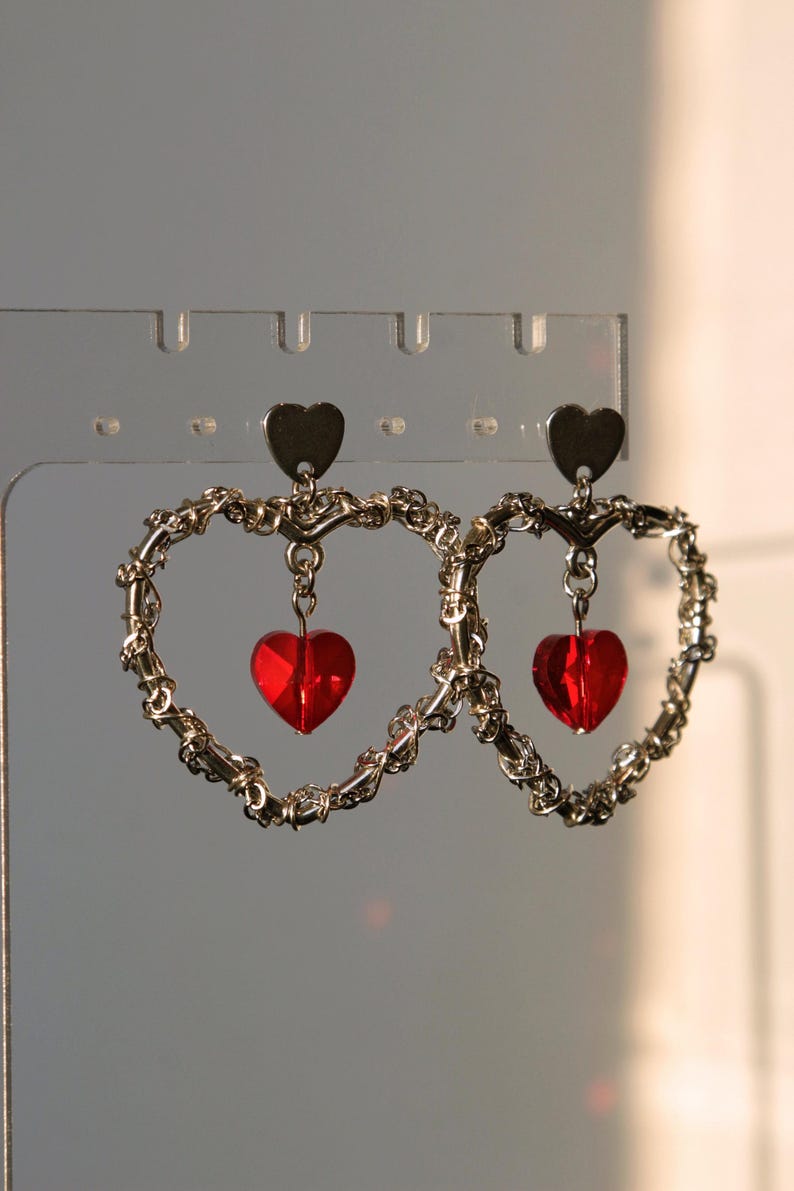 May include: A pair of silver heart-shaped earrings with dangling red heart-shaped crystals.