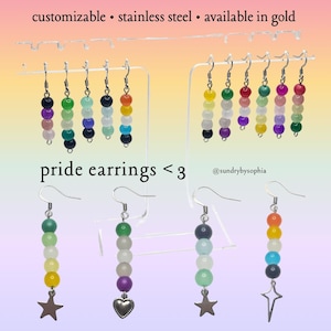 May include: A display of colorful beaded pride earrings. The earrings are in various color combinations, including rainbow and other pride flag colors. The text "pride earrings <3" is visible. The earrings are customizable, made of stainless steel, and available in gold.