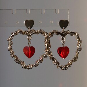 May include: A pair of gold heart-shaped earrings with dangling red heart-shaped charms.