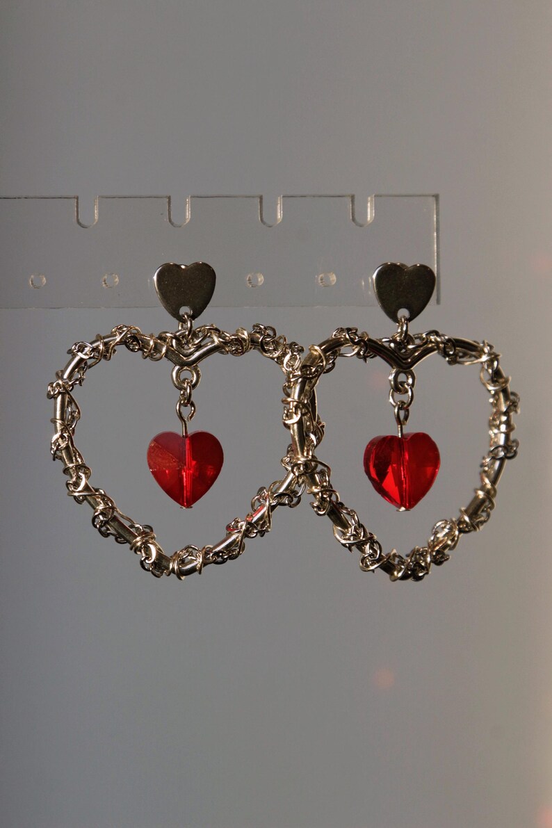 May include: A pair of gold heart-shaped earrings with dangling red heart-shaped charms.
