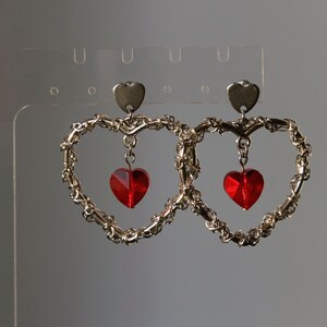May include: A pair of silver heart-shaped earrings with dangling red heart-shaped crystals.