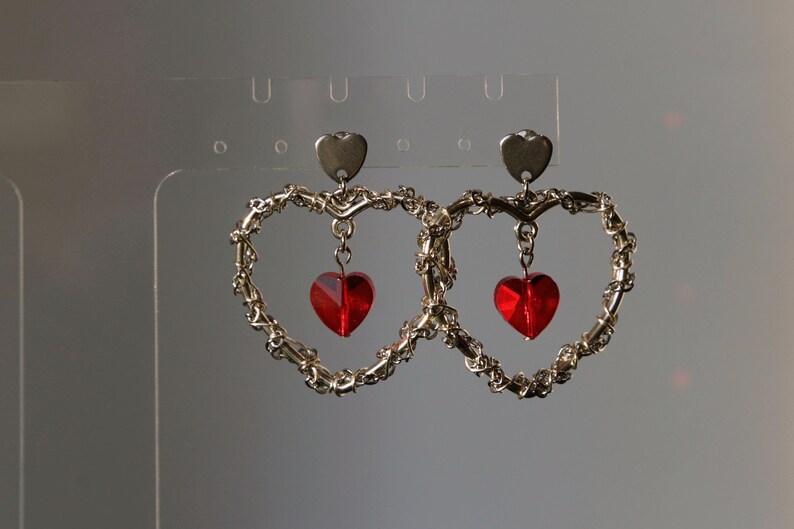 May include: A pair of silver heart-shaped earrings with dangling red heart-shaped crystals.