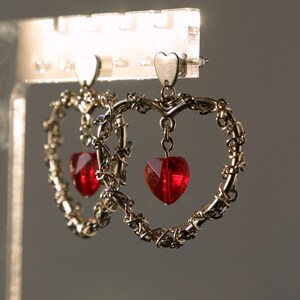 May include: A pair of silver heart-shaped earrings with dangling red heart-shaped crystals.