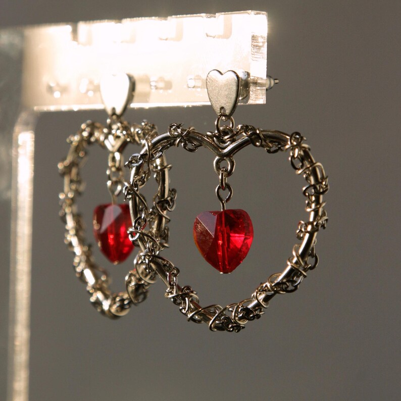 May include: A pair of silver heart-shaped earrings with dangling red heart-shaped crystals.