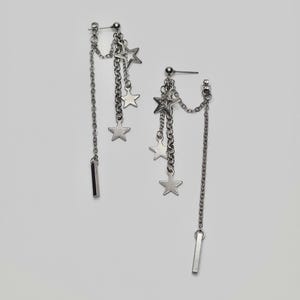 May include: A pair of silver dangle earrings with multiple star charms hanging from chains. The earrings have a bar-shaped post.