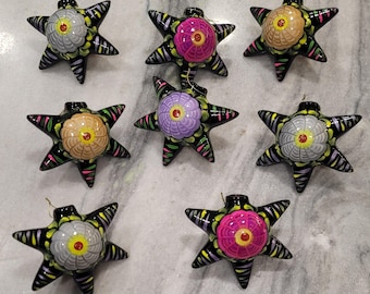 May include: Eight black star-shaped ornaments with colorful floral designs. The ornaments have a 3D effect and are painted with pink, purple, white, and yellow flowers.