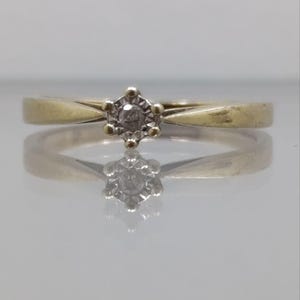 May include: A simple gold band ring with a single, small, round diamond in the center.