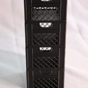 May include: A stack of four black plastic storage crates with a grid pattern. The crates are stacked on top of each other and have a handle on each side.