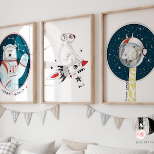 May include: Three framed illustrations of animals in space. A polar bear wearing an astronaut suit, a koala riding a rocket, and a giraffe wearing an astronaut helmet. The illustrations are on a white background with stars and the text "Exploring the universe" and "In outer space".