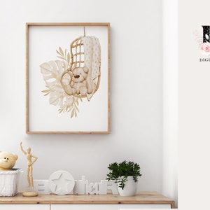 May include: A watercolor illustration of a brown teddy bear sitting in a wicker chair with a white and brown patterned cushion. The bear is surrounded by beige and brown leaves and plants. The illustration is framed in a light brown frame.