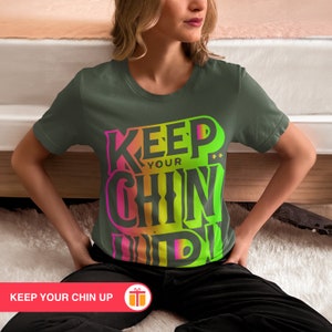 May include: A dark green t-shirt with a colorful graphic that says "Keep Your Chin Up".