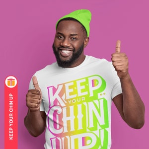May include: A white t-shirt with a colorful graphic that says "Keep Your Chin Up!" The graphic is in a rainbow gradient of pink, yellow, green, and blue. The person wearing the shirt is smiling and giving a thumbs up.