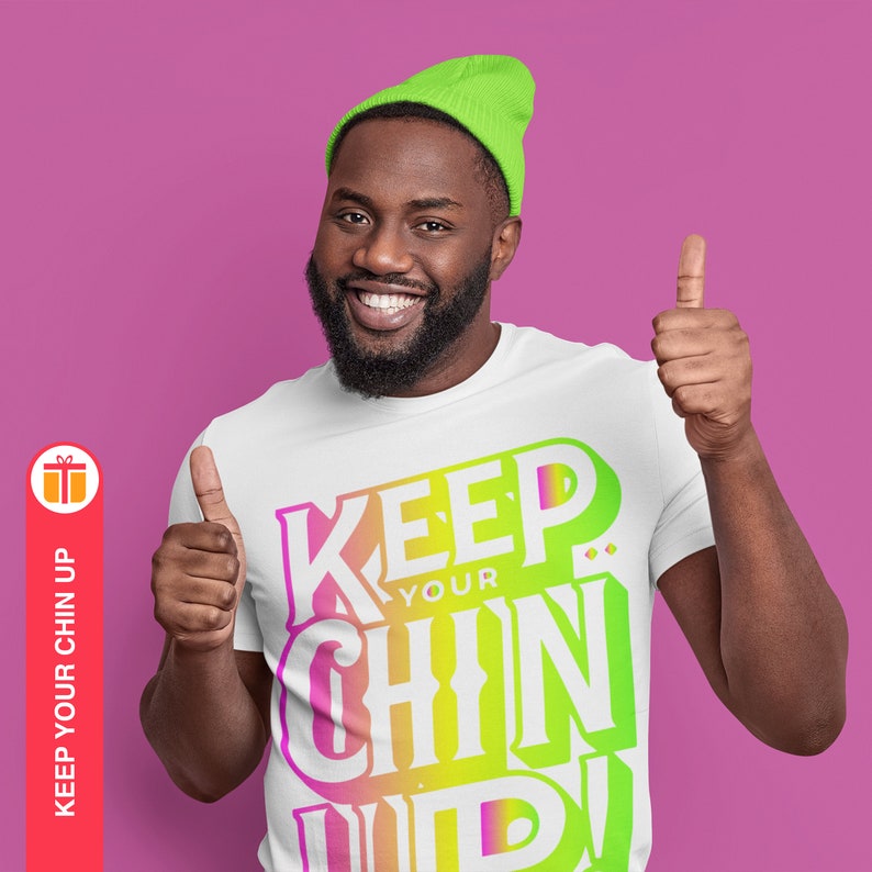 May include: A white t-shirt with a colorful graphic that says "Keep Your Chin Up!" The graphic is in a rainbow gradient of pink, yellow, green, and blue. The person wearing the shirt is smiling and giving a thumbs up.