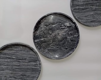 May include: Three round, gray marble trays with a polished finish. The trays have a natural, swirling pattern of light and dark gray, creating a unique look. The trays are of varying sizes and are displayed against a white background.