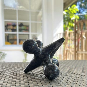 May include: A black, star-shaped,  stone paperweight with rounded edges. The paperweight is made of a dark, mottled stone.