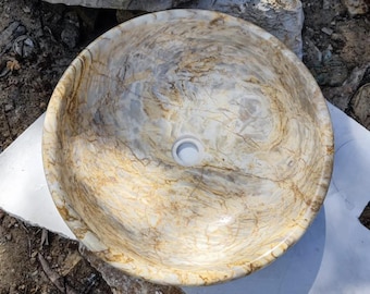 Könnte beinhalten: Ein rundes, weißes Steinkessel mit einem braunen und goldenen Marmormuster. Das Waschbecken hat ein kreisförmiges Abflussloch in der Mitte.