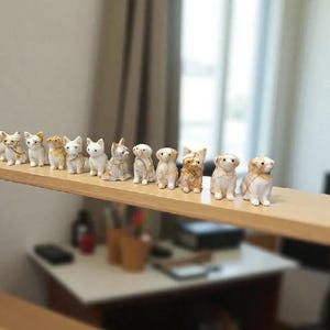 May include: A collection of small ceramic cat and dog figurines, arranged on a wooden shelf. The figurines are primarily white with gold accents, depicting various breeds and poses. The shelf is part of a larger wooden structure, with a blurred background.