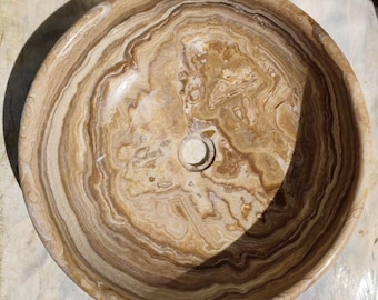 Könnte beinhalten: Ein rundes, braunes und weißes Onyx-Steinwaschbecken mit einem runden Abflussloch in der Mitte. Das Waschbecken hat ein wirbelndes Muster aus hell- und dunkelbraun.