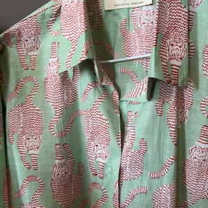 May include: A green button-up shirt with a red tiger print. The shirt has a label that reads "The Jaipur Label, Handcrafted Creations".