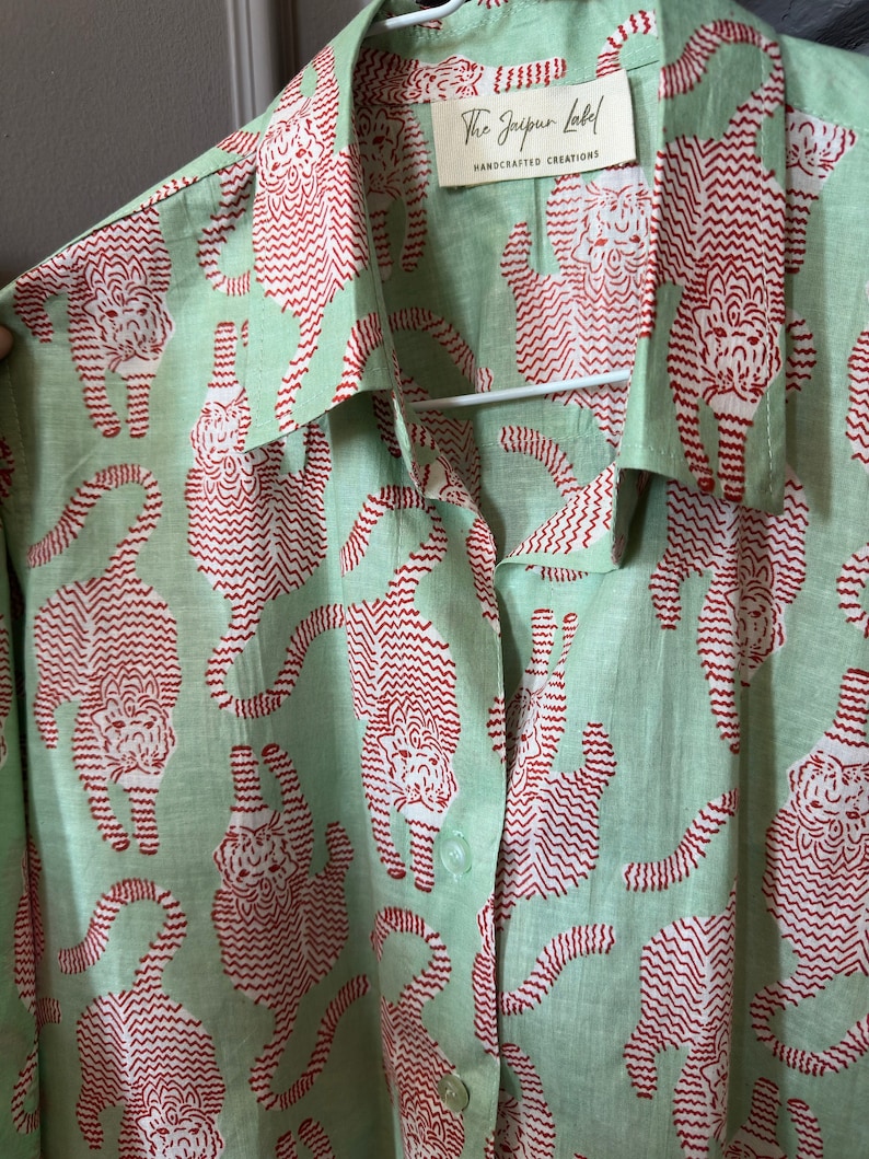 May include: A green button-up shirt with a red tiger print. The shirt has a label that reads "The Jaipur Label, Handcrafted Creations".