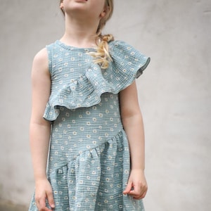 May include: A light blue dress with a white floral pattern. The dress features a ruffled shoulder detail and a tiered skirt. The fabric appears to be a lightweight cotton or linen. The dress is sleeveless and suitable for warm weather.