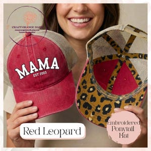 May include: Two red trucker hats with mesh backs are held up. One hat has the word "MAMA" in white block letters and "EST 2003". The other hat has a leopard print design on the underside. The text "Red Leopard" is at the bottom.