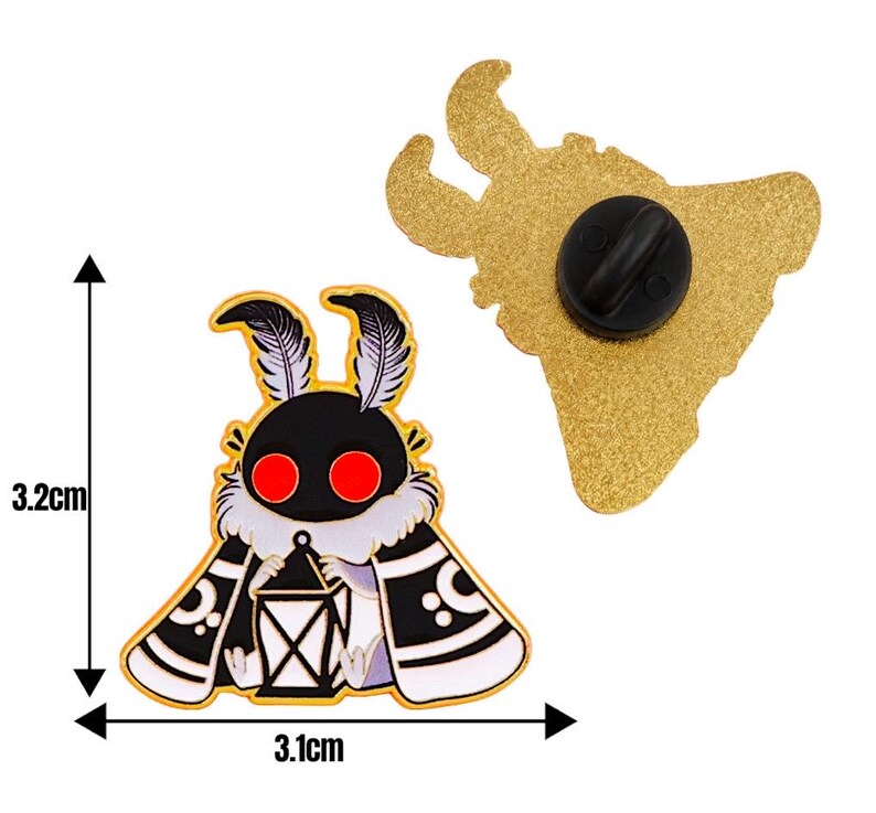 May include: A moth-shaped enamel pin, 3.2 cm high and 3.1 cm wide, featuring a black head, red eyes, and a white and black patterned cape. The pin's reverse is gold with a black pin clasp.